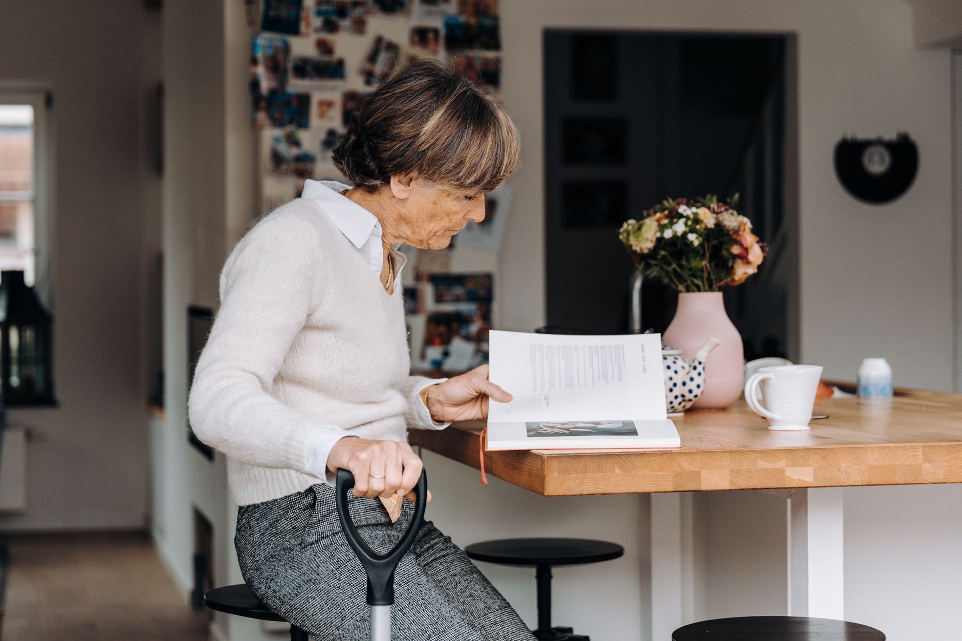 pexels-photo-33061526 senior woman reading book in cozy kitchen interior
