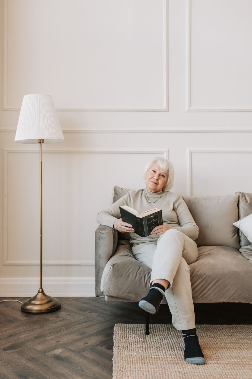 elderly woman sitting on gray sofa holding a book