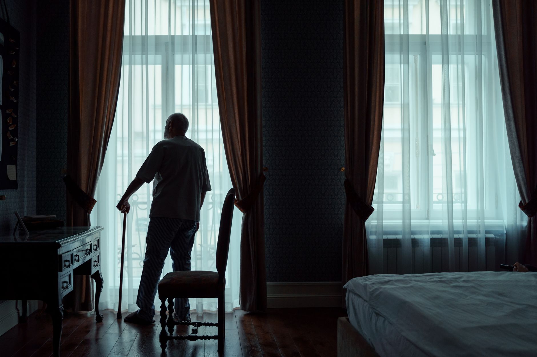 back view of an elderly man standing in front of the window